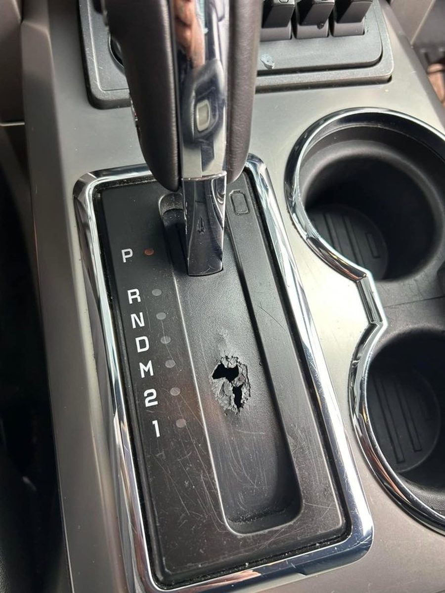 A factory Ford shifter bezel cracked through, with a hole worn open beside the shift gate.